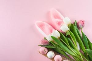 Happy Easter holiday background concept. White tulips flowers, bunny ears, easter eggs. Flat lay photo