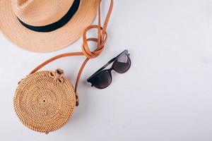 concepto de moda de viajes de verano femenino. bolsa de paja, bolsa de mimbre redonda, gafas de sol sobre fondo blanco foto