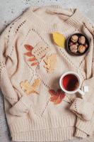 Flat lay with cup of tea, note with text hello aututmn colorful autumn leaves, nuts on sweater. photo
