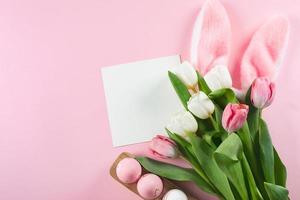 composición plana de Pascua. huevos de pascua, tarjeta vacía en blanco y tulipanes blancos. tarjeta con lugar para el texto. foto