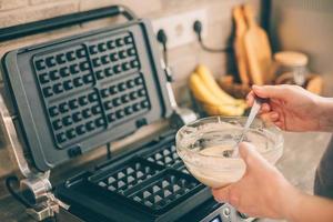 Young woman preparing Belgian waffles in the kitchen. Cooking process photo