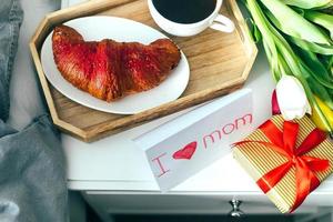 Breakfast cup of coffee, croissant served in wooden tray with gift present and tulips. Mother's day concept photo