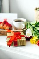 Close-up of gify box and fresh tulips for Morher's day. Romantic surprise with tasty breakfast photo