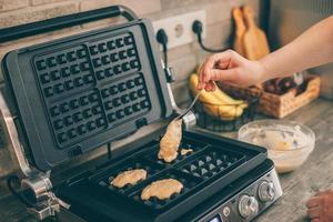 Young woman preparing Belgian waffles in the kitchen. Cooking process photo