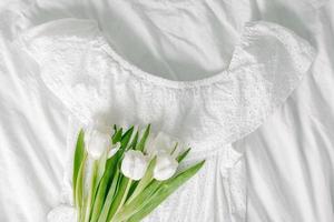 White cotton summer dress, bouquet of tulups. Top view. Concept of spring, summer outfit. Still life photo