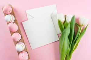 composición plana de Pascua. huevos de pascua, tarjeta vacía en blanco y tulipanes blancos. concepto de maqueta. foto