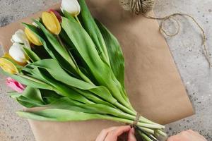 tulipanes blancos y amarillos en un paquete de artesanía. manos femeninas arreglando un ramo de flores en papel artesanal. concepto de vacaciones de primavera foto