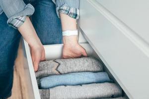 A woman folds clothes sweaters in drawer. Concept of clothes storage, minimalism lifestyle photo