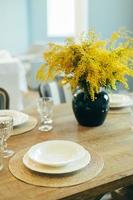 Wooden table with empty plates and glasses. Festive Easter table setting. Branches of mimosa in vase photo