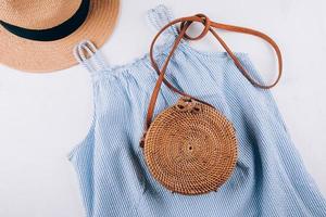 Blue summer dress, organic round bag, straw beach hat. Casual clothes for summertime. Flat lay photo