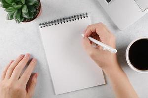 manos de mujer escribiendo para hacer una lista o planes en un cuaderno en el escritorio de la oficina. vista superior, espacio de copia foto