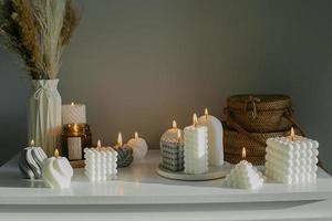 decoración interior del hogar. tocador blanco con flores secas en jarrón, bolsas de mimbre y velas variadas. bodegón, concepto hygge foto