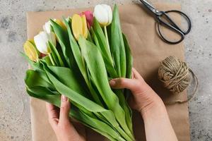 White and yellow tulips in a package of craft. Female hands arranging a bouquet of flowers in craft paper. Spring holidays concept photo