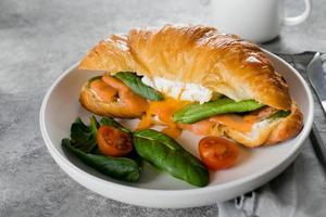 Croissant sandwich with cottage cheese, salmon, spinach. poached egg. Healthy breakfast. photo