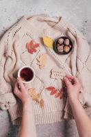 manos de mujer sosteniendo una taza de té y tarjeta de felicitación hola otoño. acogedor suéter beige. foto