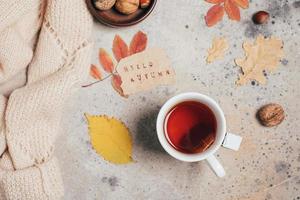 Flat lay with cup of tea, note with text hello aututmn colorful autumn leaves, nuts, cozy sweater photo