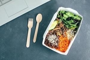 Office desk with laptop and reusable paper container with healthy lunch. Top view photo