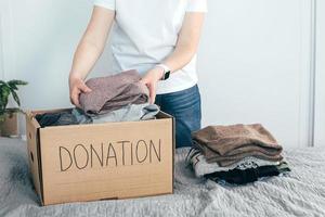 concepto de donación. mujer joven en camiseta blanca con caja de donación en casa. mujer dona ropa foto