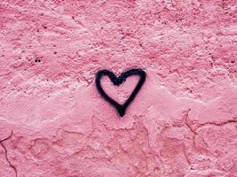 corazón dibujado con pintura en aerosol negra en una pared rosa dañada foto