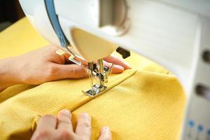 Female hands stitching yellow fabric on modern sewing machine. Close up view of sewing process. photo