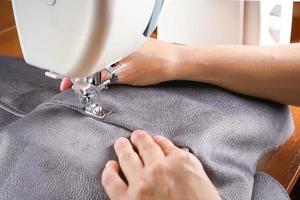 Female hands stitching gray fabric on modern sewing machine. Close up view of sewing process. photo