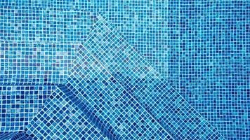 The light reflected on the top of the water surface of the pool lined with blue mosaic tiles below. Water ripples on blue-tiled swimming pool background. photo