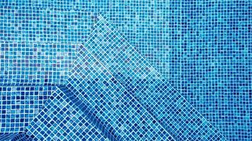 la luz reflejada en la parte superior de la superficie del agua de la piscina revestida con mosaicos azules debajo. ondas de agua en el fondo de la piscina de azulejos azules. foto