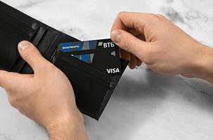 Men's hands hold a wallet with a plastic Visa bank card of the Russian VTB in the wallet. Chelyabinsk, Russia 06.01.2023 photo