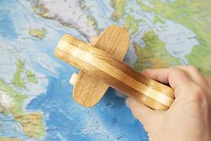 A man's hand holds a wooden toy model of an airplane against the background of a world map. The concept of travel and vacation. photo