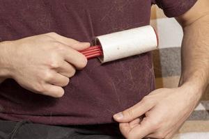 A man with a sticky clothes roller removes animal hair from clothes. Cat hair on clothes. A sticky roller that removes cat hair. photo