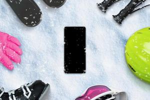 Phone on snow surrounded by ski equipment. Blank screen with snowflakes for app design presentation, mockup.  Top view, flat lay composition photo