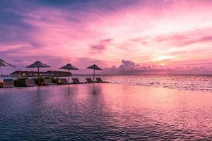 sombrilla y silla alrededor de la piscina infinita cerca de la playa del océano al amanecer o al atardecer. para viajes de ocio y concepto de vacaciones, paisaje de veraneo. vacaciones de relajación tropical, puesta de sol foto