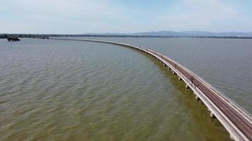 vista aérea de um incrível trem de viagem estacionado em uma ponte ferroviária flutuante sobre a água do lago na represa pa sak jolasid com céu azul em lopburi, tailândia. video