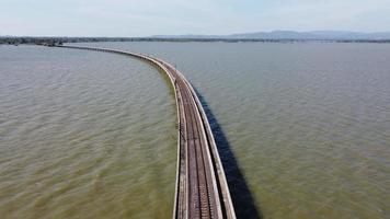 Aerial view of an amazing travel train parked on a floating railway bridge over the water of the lake in Pa Sak Jolasid dam with blue sky at Lopburi, Thailand. video