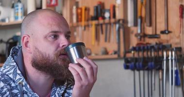 Carpenter in the workshop drinks tea with a sandwich against the background of a hand tool. Slow motion video