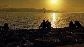 persone seduta su pietre su il spiaggia e guardare a il mare video