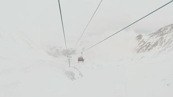 lasso di tempo di bianca rosso chiuso sciare sollevamento cabine nel veloce movimento su cavo corda con sciatori nel nevoso giorno. sciare ricorrere riapre. Georgia inverno vacanze nel gudauri. kobi versante freeride video