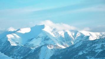 vergrößern sie im hintergrund zeitrafferaufnahme von fliegenden wolken über schneebedeckten kazbegi kaukasus berggipfeln während eines sonnigen tages und eines klaren blauen himmels video