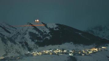 aumentar o zoom do dia para a noite stepantsminda, georgia. céu estrelado de noite de inverno com estrelas brilhantes sobre o pico do monte kazbek coberto de neve. bela noite georgiana paisagem de inverno video