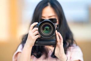 gafas de sol amateur mujer asiática toma una foto con una cámara profesional sin espejo en el edificio de la azotea azul al aire libre en el crepúsculo.
