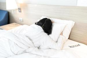 Asian Lady in white long arm t-shirt pajamas lie prone, lie on the stomach in bed with tried and exhausted mood and tone. photo