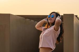 una chica de pelo largo con gafas asiáticas está bailando en la azotea del edificio al atardecer. foto