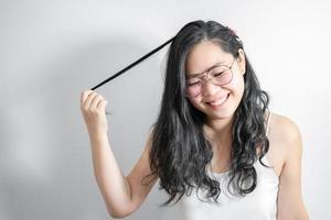 una chica tímida asiática feliz y sonríe jugando con su cabello en un estudio de fondo blanco claro. foto