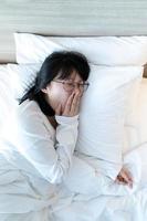 anteojos mujer asiática está bostezando después de despertarse en la cama por la mañana. foto