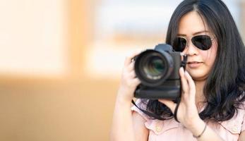 gafas de sol amateur mujer asiática toma una foto con una cámara profesional sin espejo en el edificio de la azotea azul al aire libre en el crepúsculo.