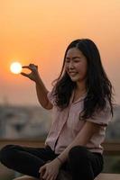 mujer tailandesa china asiática juega con la forma del sol en la azotea en el crepúsculo. foto