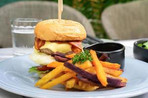 Burger homemade on the white dish with Bacon and Cheese is served with purple Sweet Potato fried in restaurant, Fresh American Food. photo