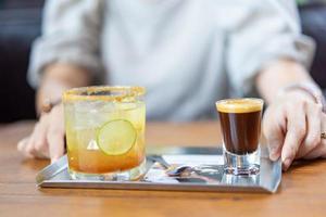 una combinación entre café recién hecho, limón, refresco de naranja en el plato de acero inoxidable en la mesa de madera frente a la mujer borrosa en el café. foto