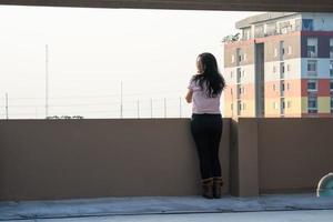una adolescente asiática se encuentra en la parte trasera frente a la vista de la ciudad en la azotea del edificio foto