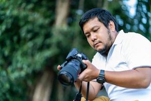 cámara profesional tailandesa de barba asiática ver imagen tomada a través de liveview detrás de una cámara sin espejo de formato medio con fondo de árbol verde. foto